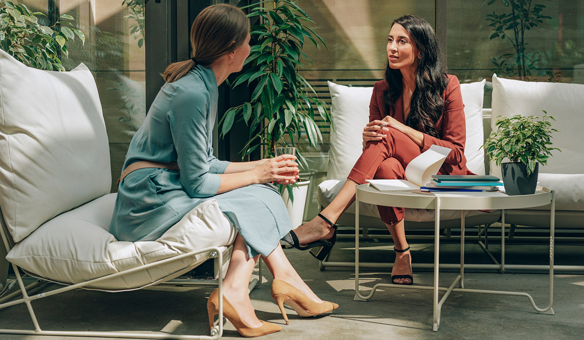 A businesswoman sitting and chatting with her colleague. Image credit: Stocksy