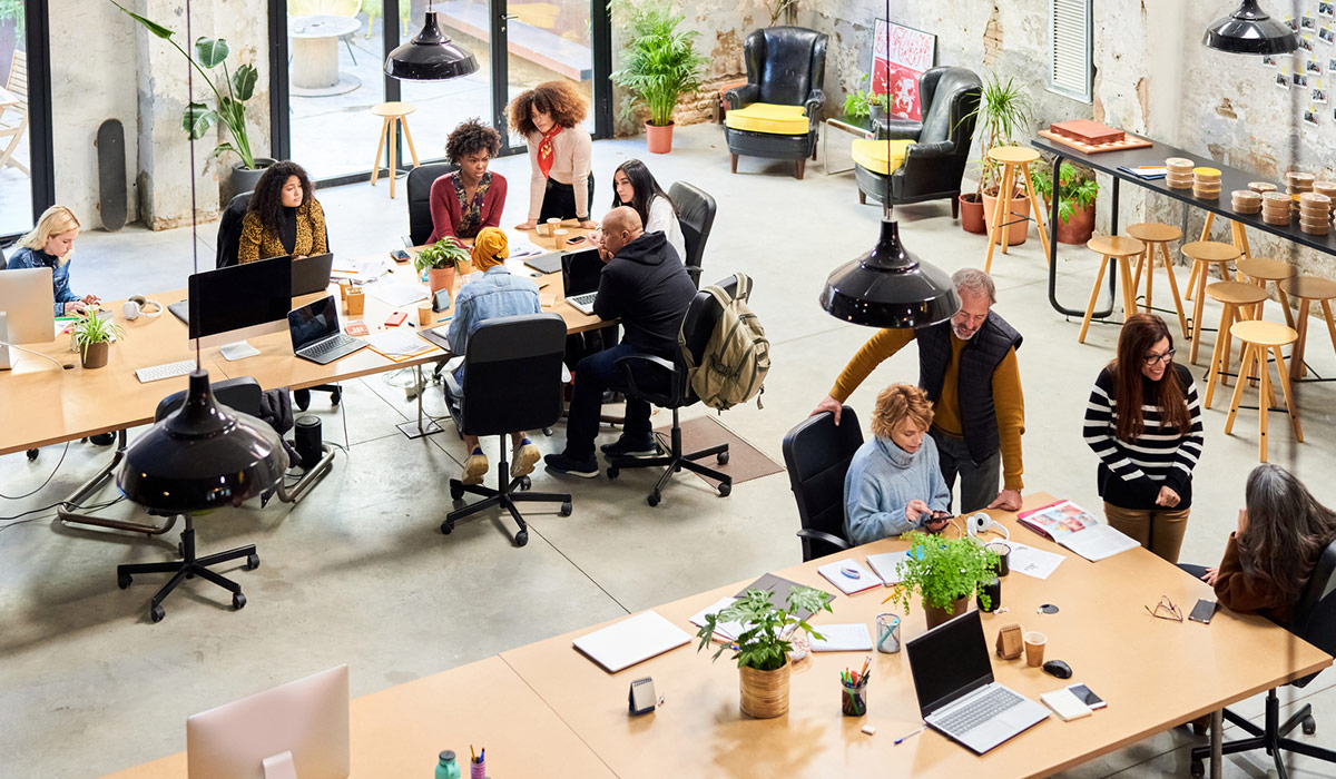 Aerial shot of a busy and trendy office with people sat at their desks busy working. Image credit: Stocksy